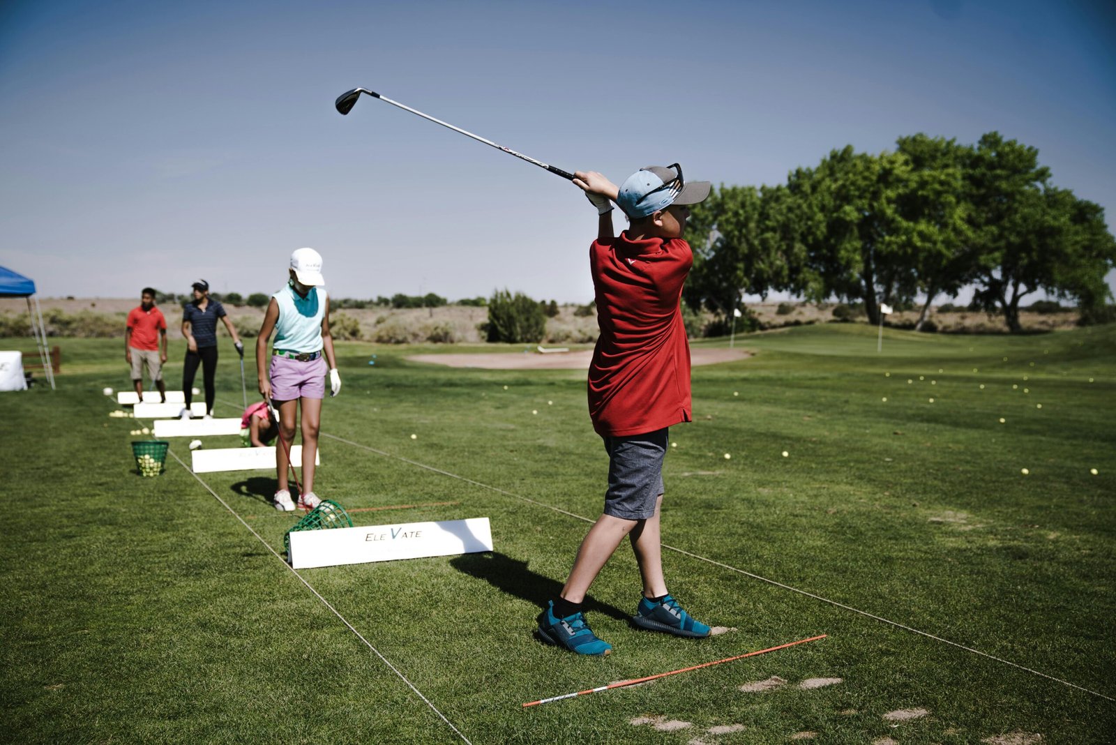 A group of youth practicing golf swings on a sunny day at the driving range.